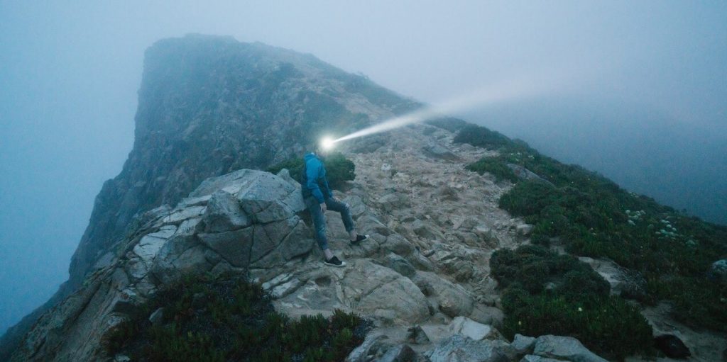 Hiker in a mountain surrounded by fog, wearing a headlamp for visibility.